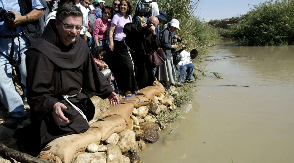 José Rodriguez Carballo, head of the Catholic Franciscan order, kneels at the Jordan River at Qasr al-Yehud, where Jesus is believed to have been baptized, Oct. 30, 2003. Photo by David Silverman/Getty Images.