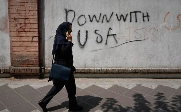 A woman talks on her cellphone as she walks past an anti-US graffiti on the wall of the British Embassy in Tehran, Iran, July 27, 2026. (AP Photo/Vahid Salemi)