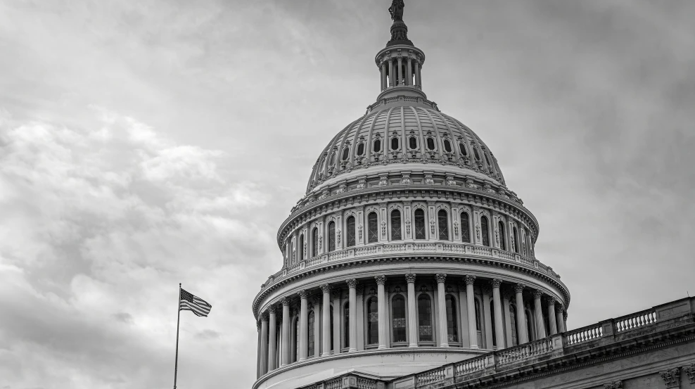Black and white photo of the United States Capitol building with the American flag blowing in the wind in Washington, D.C., Dec. 10. 2025. Credit: Sgt. Eli Baker/U.S. Army.