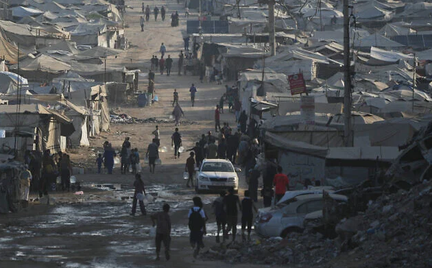 Palestinians walk among tents and rubble on the coastal road in Gaza City, in the Strip's north, on August 13, 2026. (AP Photo/Abdel Kareem Hana)