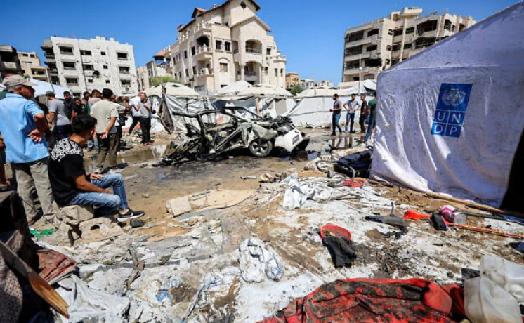 People gather near a destroyed vehicle following an Israeli strike in the Rimal neighborhood of Gaza City on September 1, 2026. (Omar AL-QATTAA/AFP)