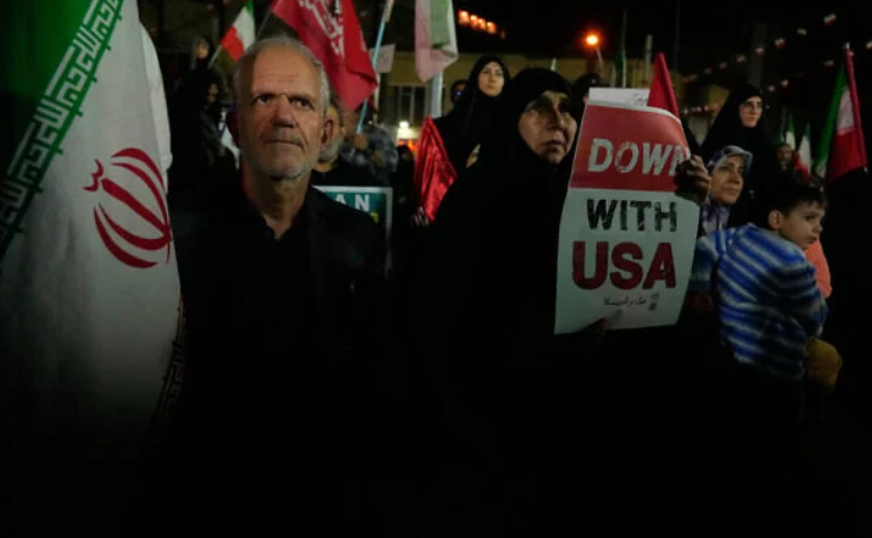 A demonstrator holds an anti-US placard as another holds an Iranian flag during a pro-government gathering in Tehran, Iran, October 27, 2026. (AP Photo/Vahid Salemi)